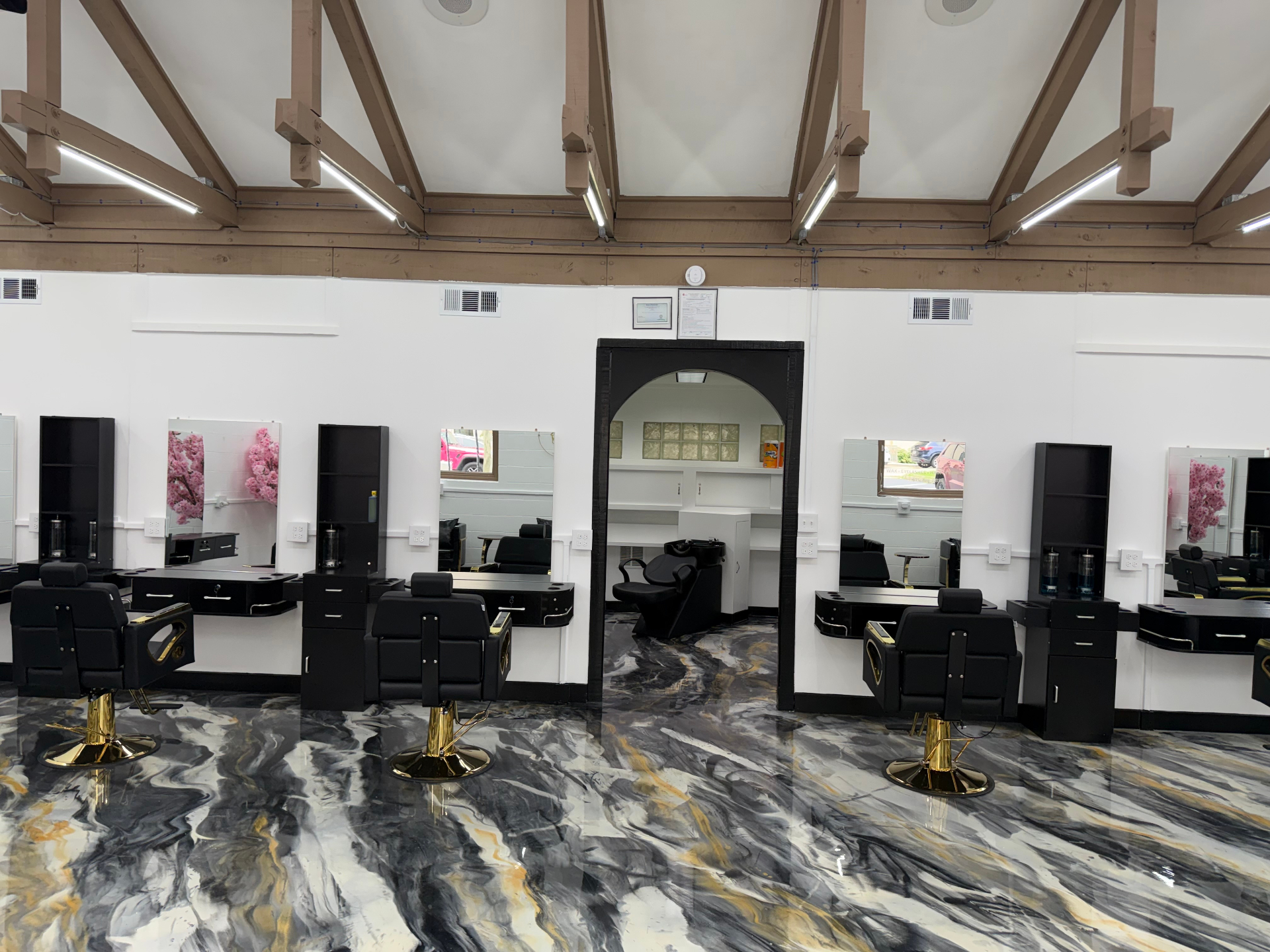 Queen Salon & Beauty interior showing black styling stations, gold-accented chairs, exposed beams, and marble flooring